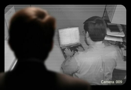 Man observing an employee work via a closed-circuit video monitor